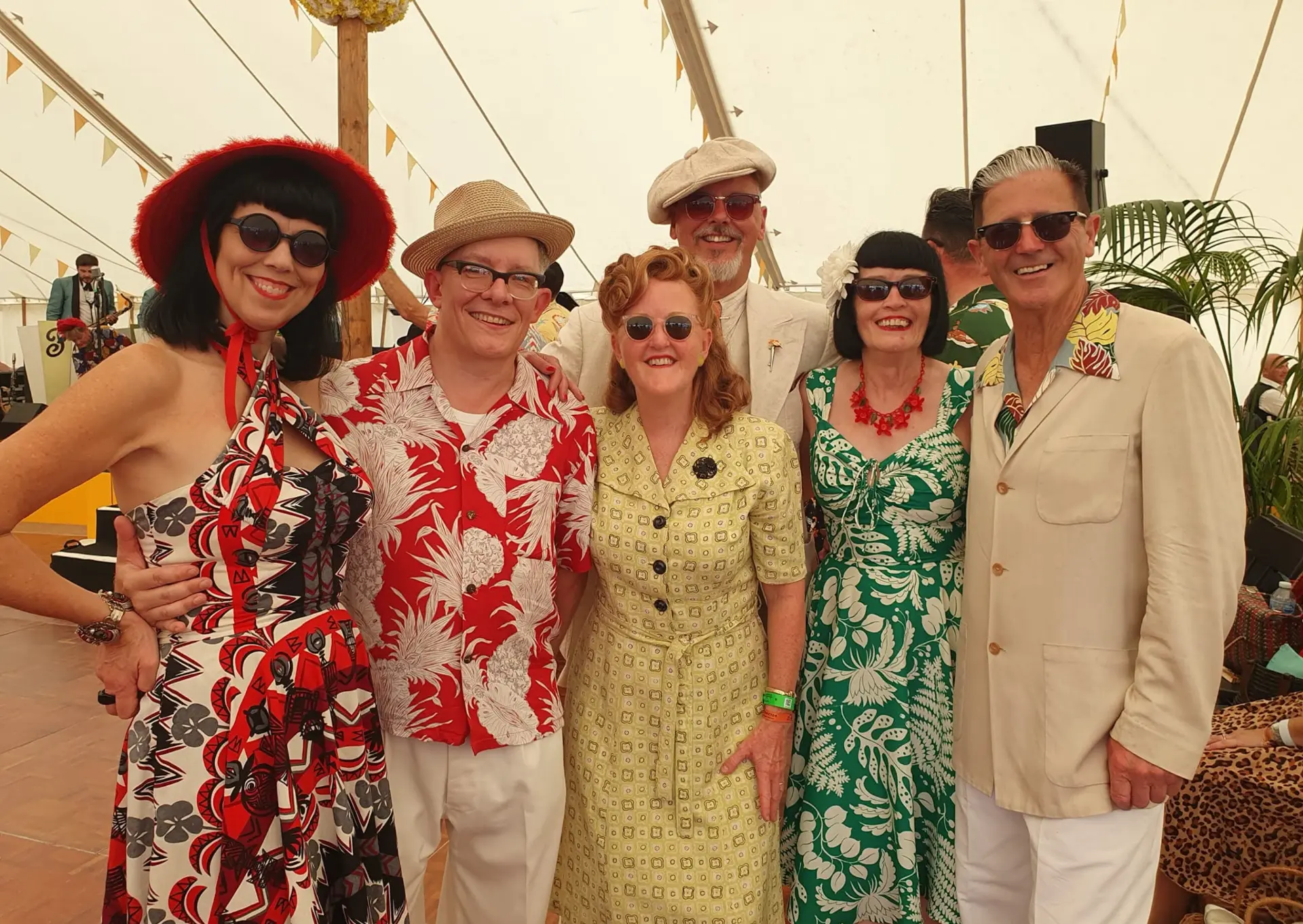 Six dancers in colourful 1940s vintage dress smiling together at a vintage motoring festival