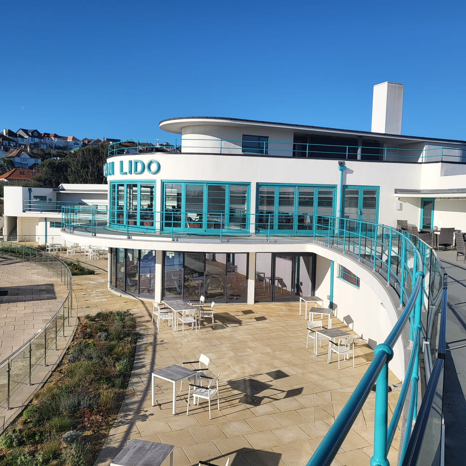 The curved white and turquoise art deco exterior of Saltdean Lido under a clear blue sky