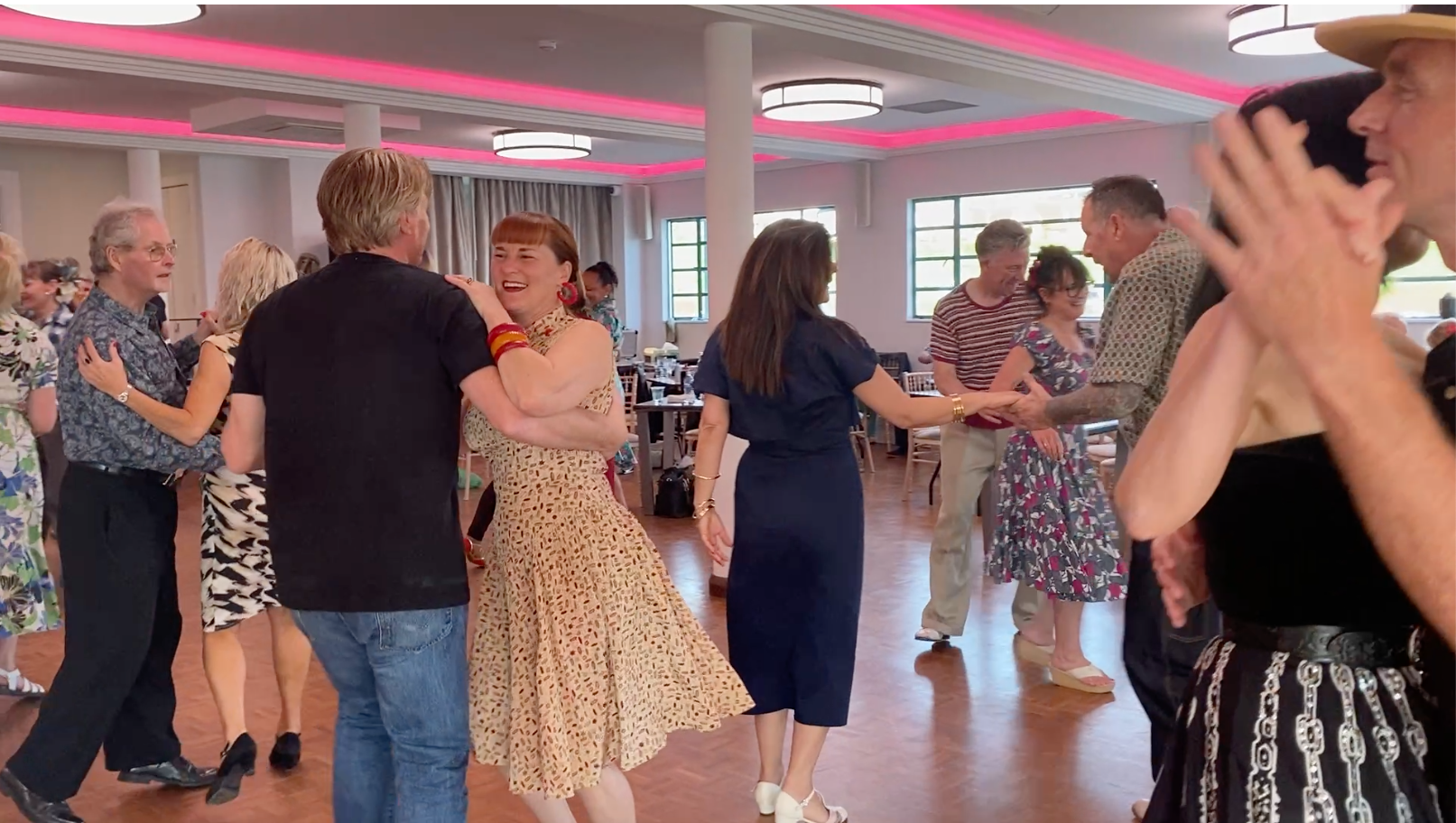 Couples dancing Lindy Hop close together, laughing, on a social dance floor