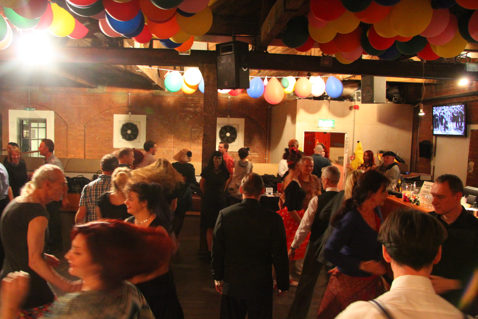 A packed evening swing dance in a brick-walled hall decorated with bunting of balloons